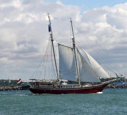 Zweimastiges Segelschiff mit schwarzem Rumpf, im Hintergrund eine aus Felsbrocken gebaute Mole 