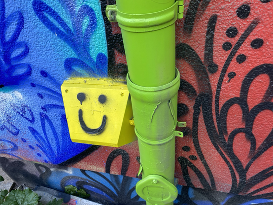 Bunte wand mit gelbem Smiley und grüner Regenrinne