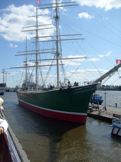 Segelschiff mit grünem Rumpf, liegt an einem Ponton im Hafen.