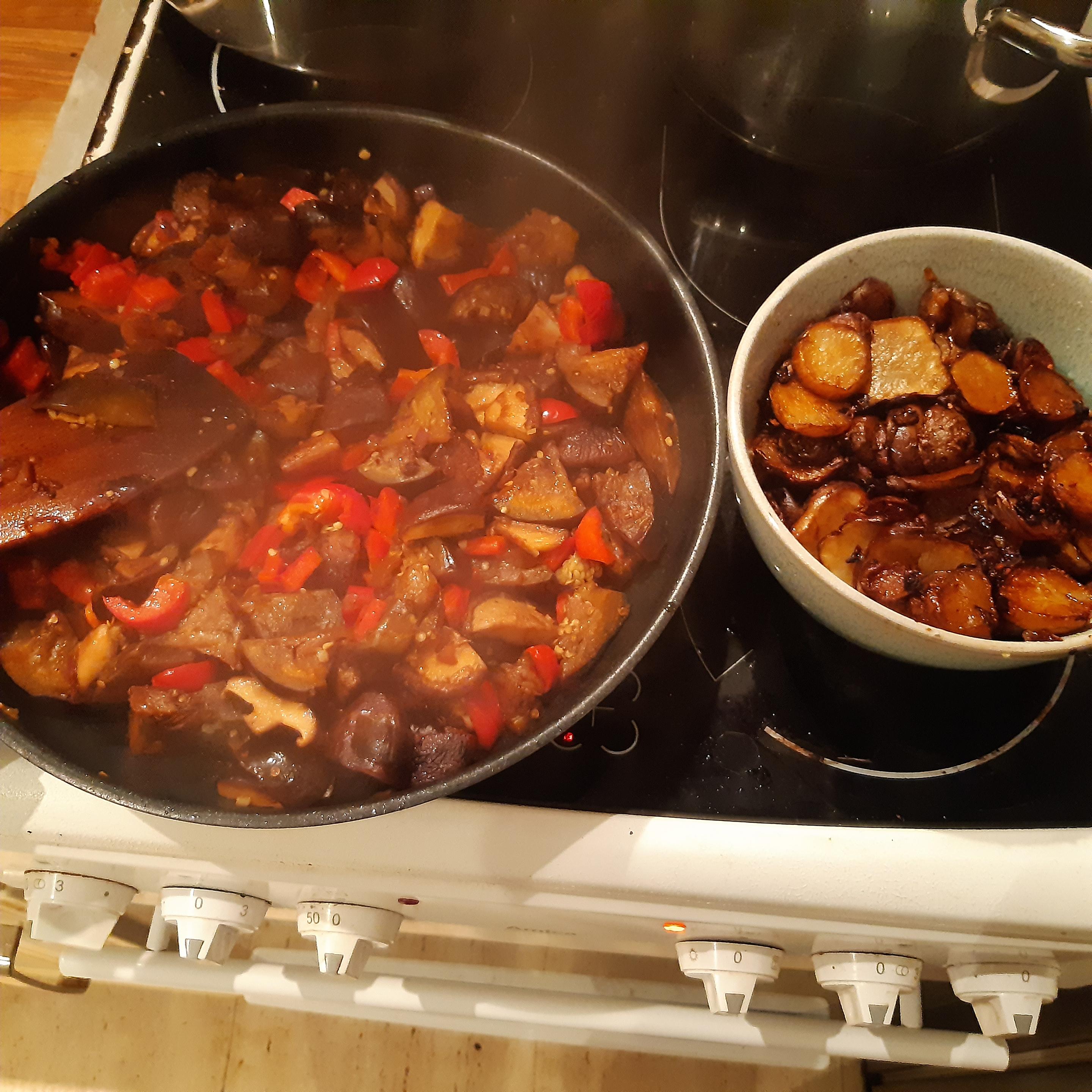 In einer Pfanne auf der linken Seite des Herds braten Shiitake, Aubergine, Paprika sowie Ziebel und Knoblauch in Olivenöl. Rechts daneben liegt in einer kleinen Schale bereits gebraten und in Scheiben geschnitten Topinambur - ebenfalls mit Zwiebel und Knoblauch.