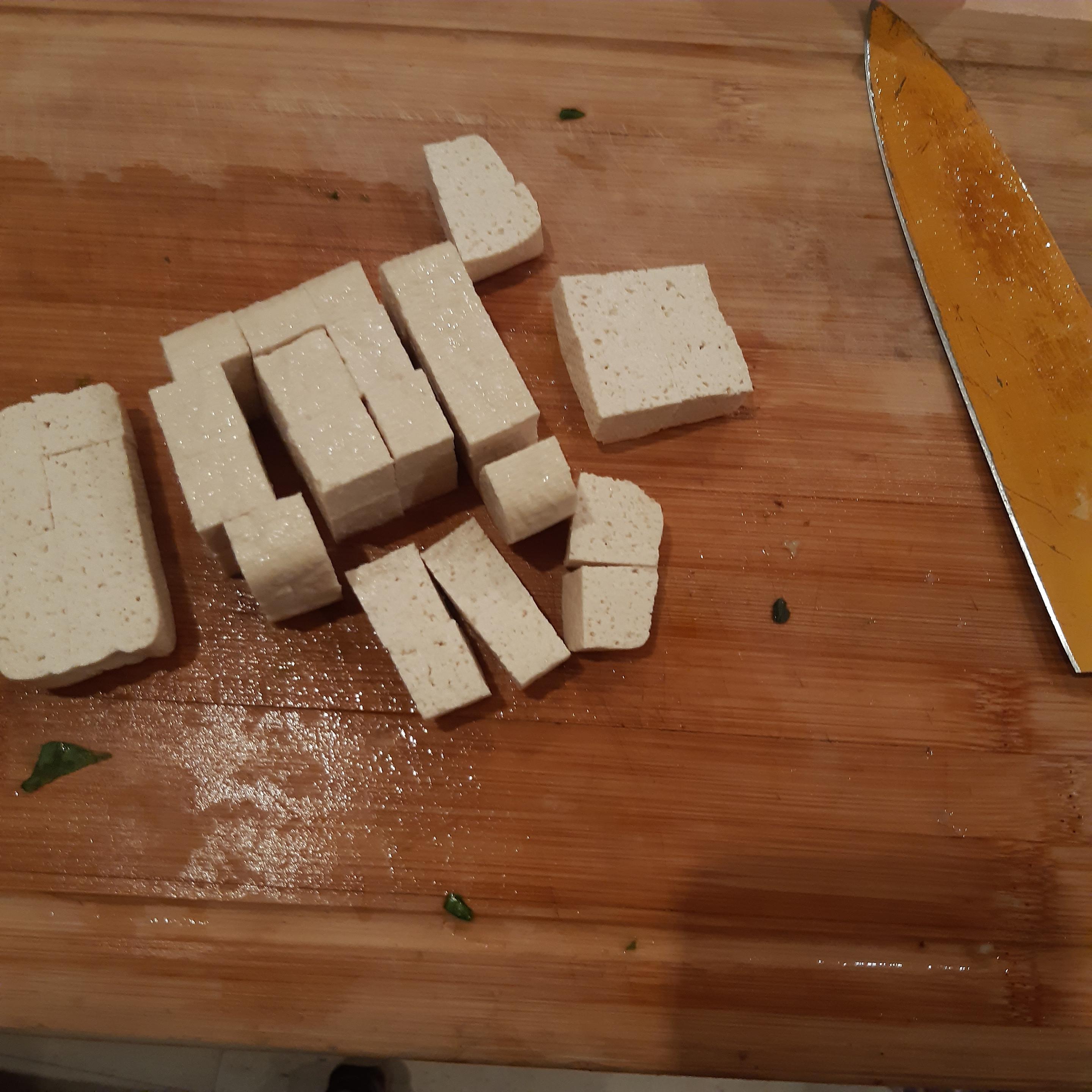 Tofu, in kleine Würfel geschnitten auf einem Küchenbrett.