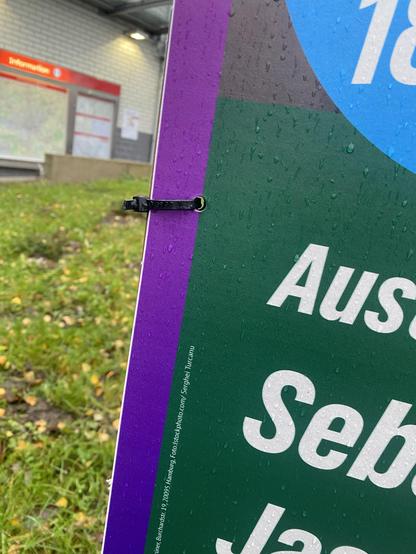 Close-up: Das Plakat ist mit Kabelbindern befestigt. Diese sind kurz abgeschnitten (also offenbar handelt es sich nicht um solche, die man wiederverwenden kann).