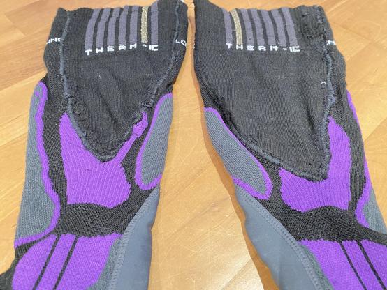 Nahaufnahme, aufgehellt. Zwei lila-schwarze Strümpfe liegen platt auf Holzfußboden. Man sieht die eingefügten Keile recht deutlich. Sie sind nicht ganz identisch.