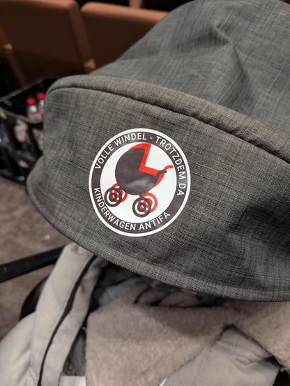 Sticker auf einem Kinderwagen mit der Aufschrift:

Volle Windel - Trotzdem da
Kinderwagen Antifa