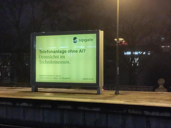 Werbetafel der Firma sipgate auf einem Bahnsteig. Darauf steht: "Telefonanlage ohne AI? Demnächst im Technikmuseum."