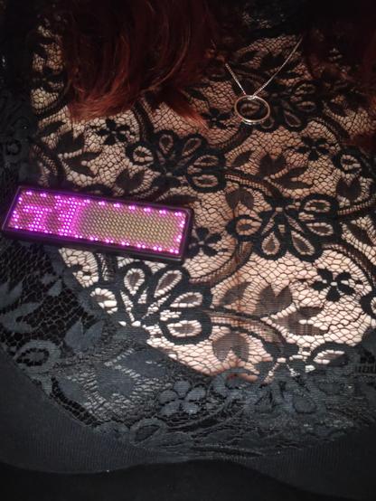 LED BADGE auf schwarzem Spitzenstoff über Dekolleté