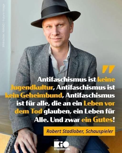 Wir sehen ein etwas älteres Kampagne-Plakat von „KiO – MDR Kultur im Osten“
Zu sehen ist auf einem Foto der Schauspieler Robert Stadlober im Anzug mit Hut wie er in die Kamera lächelt.
Drauf steht:

„Antifaschismus ist keine Jugenkultur
  Antifaschismus ist kein Geheimbund
  Antifaschismus ist für alle,
  die an ein Leben vor dem Tod glauben,
  ein Leben für Alle. 
  Und zwar ein Gutes“