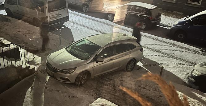 Eine verschneite und vereiste Straße. Quer über den Fußweg ist ein Auto geparkt. Fußgänger laufen drum herum.