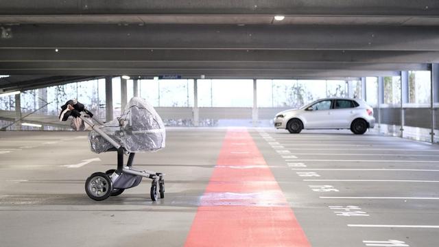 Ein fast leeres Stockwerk in einem Parkhaus. Auf dem Stockwerk steht ein Auto, alle Plätze drumherum sind ungenutzt. Im Vordergrund steht ein Kinderwagen mit Regenverdeck in einer Pfütze 