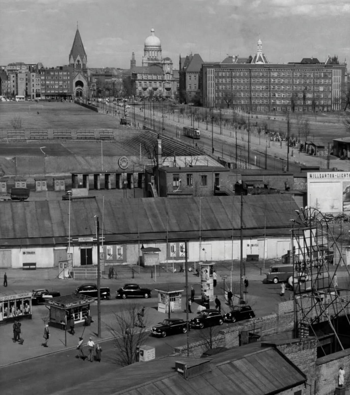 Altes Schwarzweiß-Foto. Vorne ein Fussballstadion. Hinten die Skyline von Hamburg mit einer Kirche, einer Kuppel vom Gerichtsgebäude und eine Fassade mit vielen Fenstern.
