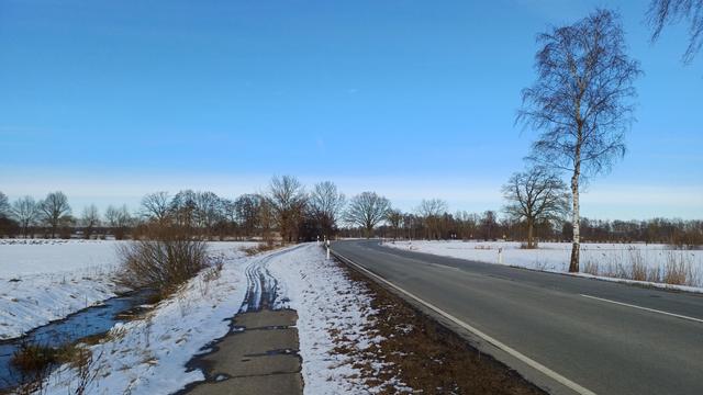 Straße, Schnee, blauer Himmel, schlecht geräumter Radweg.