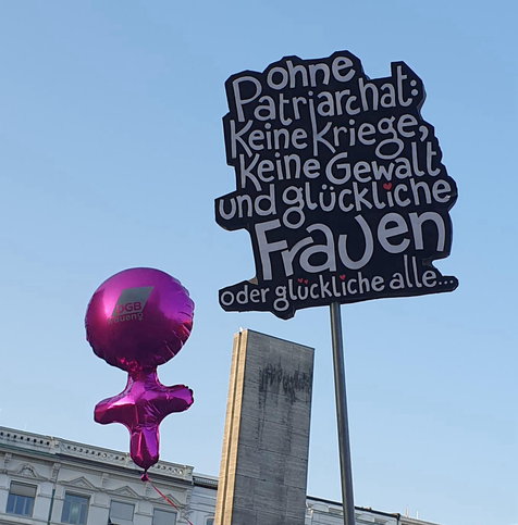 Ein lila Luftballon vom DGB in Frauenzeichenform. Und ein Schild: Ohne Patriarchat: keine Kriege, keine Gewalt und glückliche Frauen