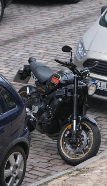 Motorrad auf der Fahrbahn am Fahrbahnrand zwischen zwei Autos geparkt.