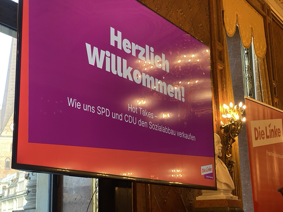 Im protzigen kleinen Saal des Hamburger Rathauses steht ein Monitor mit dem Veranstaltungstitel: Hot Takes - Wie uns SPD und CDU den Sozialabbau verkaufen.
