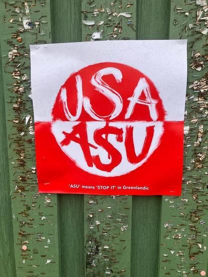 Plakat, das auf der Flagge Grönlands beruht. Im roten Halbkreis steht "USA", im weißen darunter "ASU". Eine Fußnote erklärt: "ASU means STOP IT in Greenlandic".