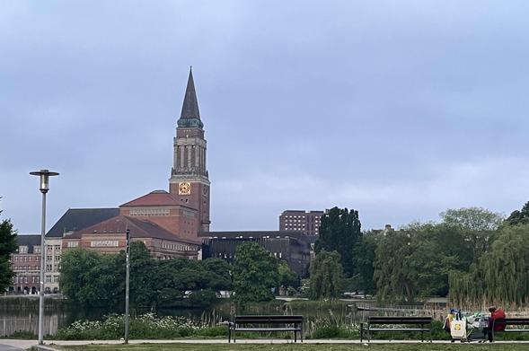 Foto über den kleinen Kiel auf Rathaus und Theater. Auf einer Bank im Vordergrund schläft ein Mensch.
