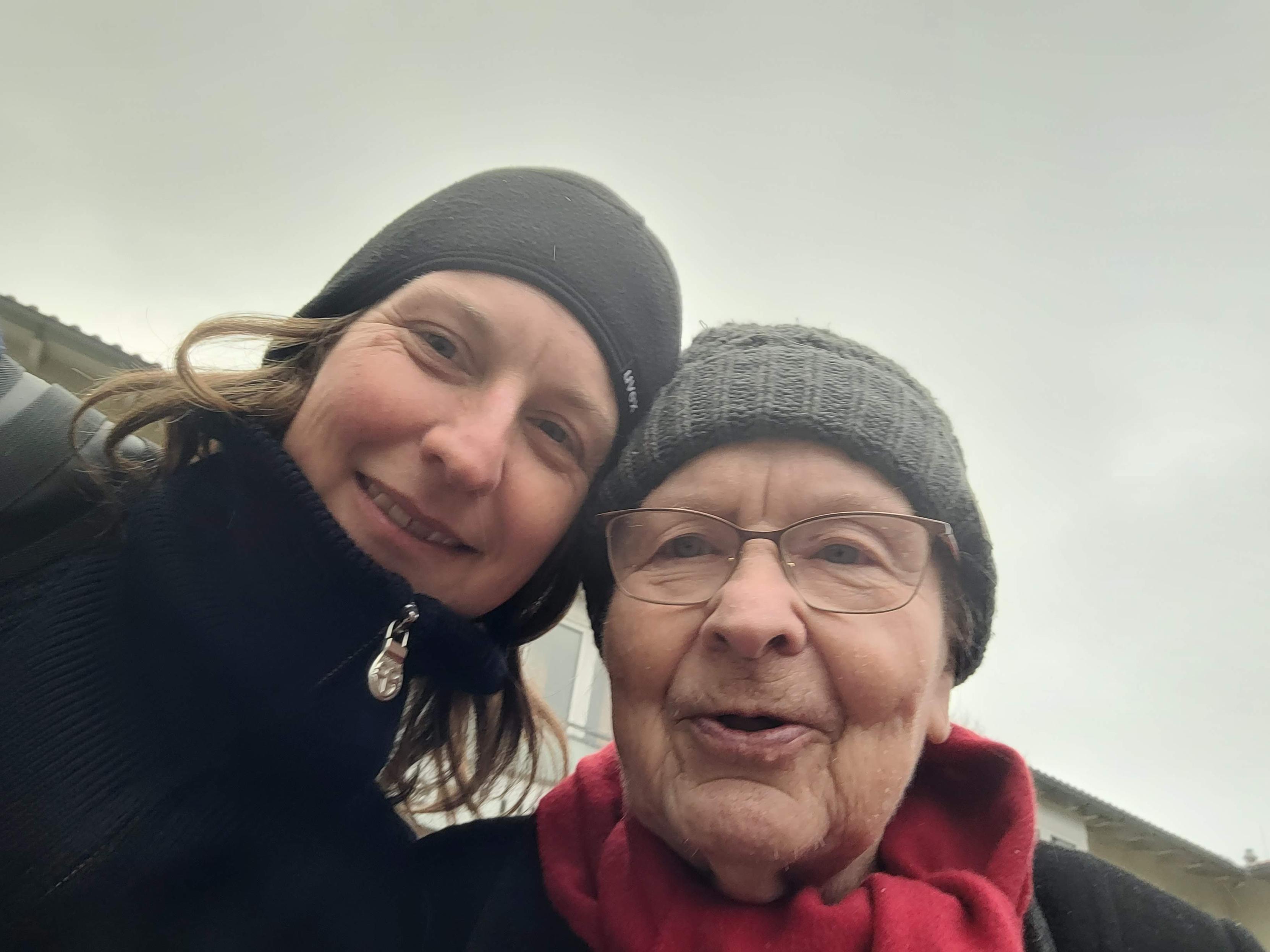 Selfie von zwei Frauen, Mutter und Tochter. Aufgenommen draußen vor grauem Himmel. Die linke Frau ist Anfang 40, die rechte Anfang 80. Beide tragen warme Kleidung und schauen freundlich.