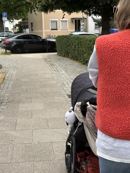 Ein Falschparker blockiert einen Fußweg in voller Breite. An Rechten Bildrand schiebt eine Person einen Kinderwagen.