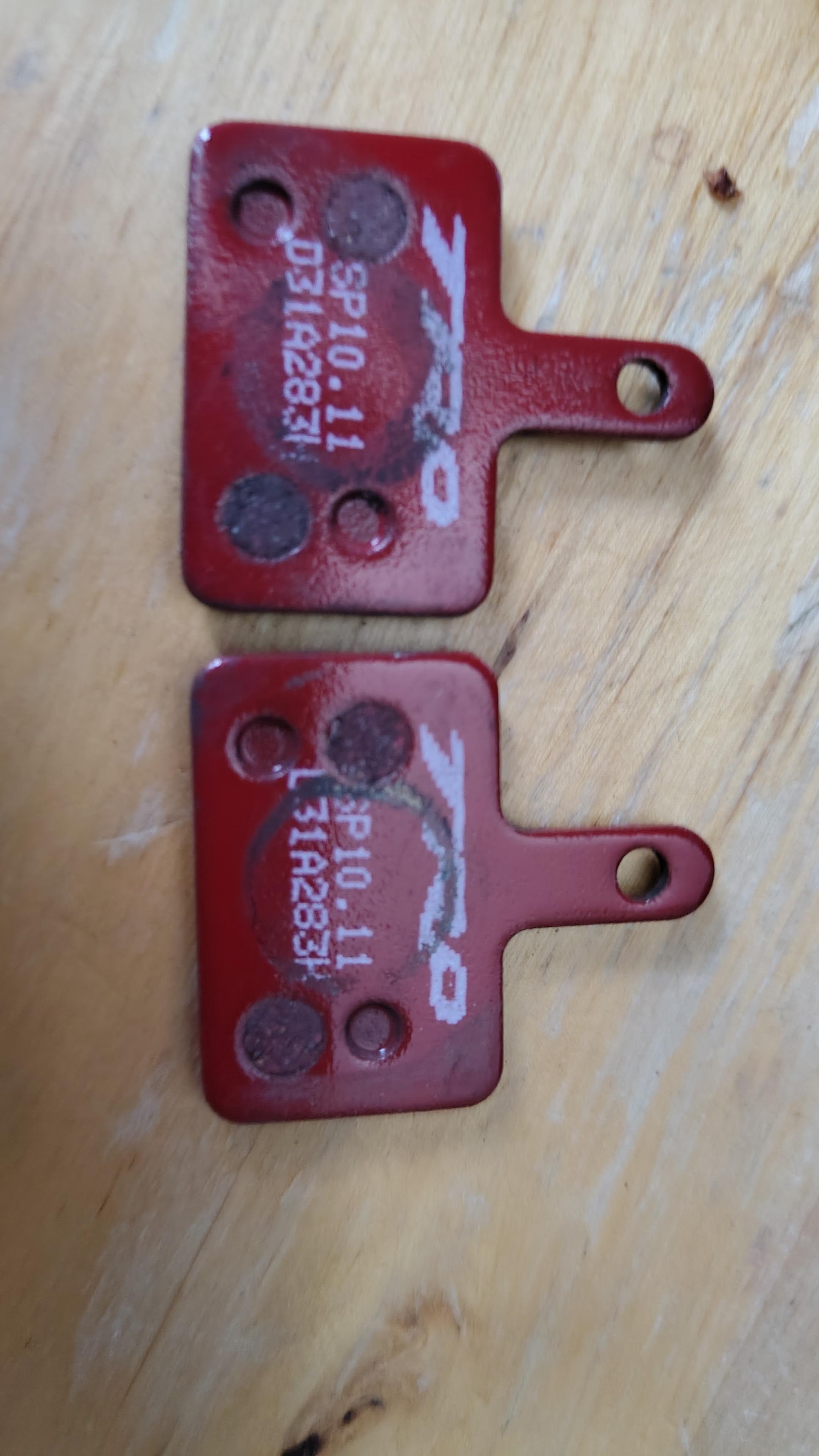 2 rote Bremsbeläge nebeneinander auf einer Holzplatte