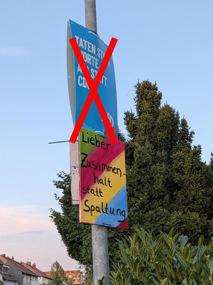 Ein handgemaltes Plakat in Regenbogenfarben und dem Spruch „Lieber Zusammenhalt statt Spaltung“ hängt an einem Laternenpfahl unterhalb eines AFD-Plakats