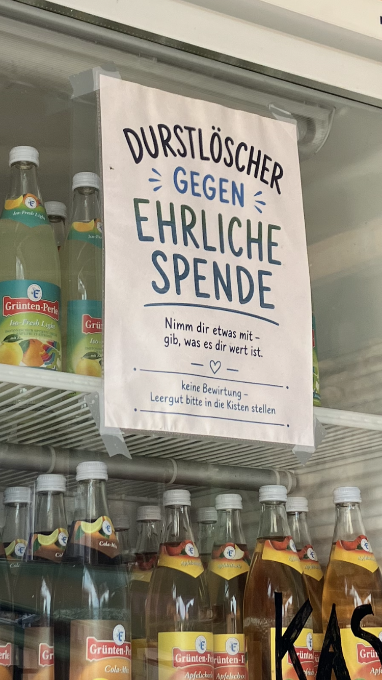Kühlschrank mit Getränken, daran ein Schild: DURSTLÖSCHER GEGEN EHRLICHE SPENDE, Nimm dir etwas mit, gib, was es dir wert ist.