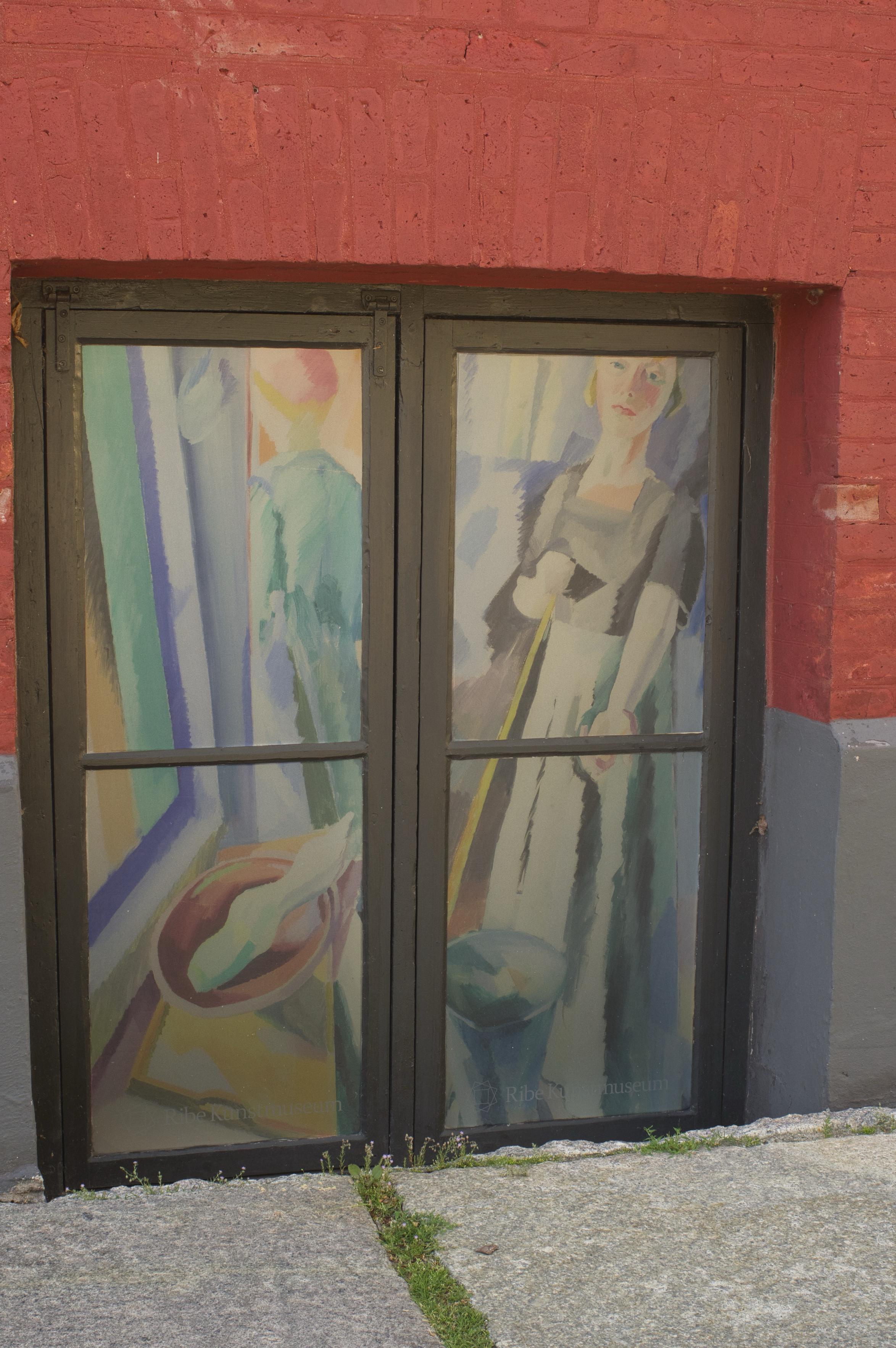 Im Foto ein weiteres Kellerfenster des Museum Ribe. Im Fenster ein Bild einer Frau. Sie scheint sauber zu machen.