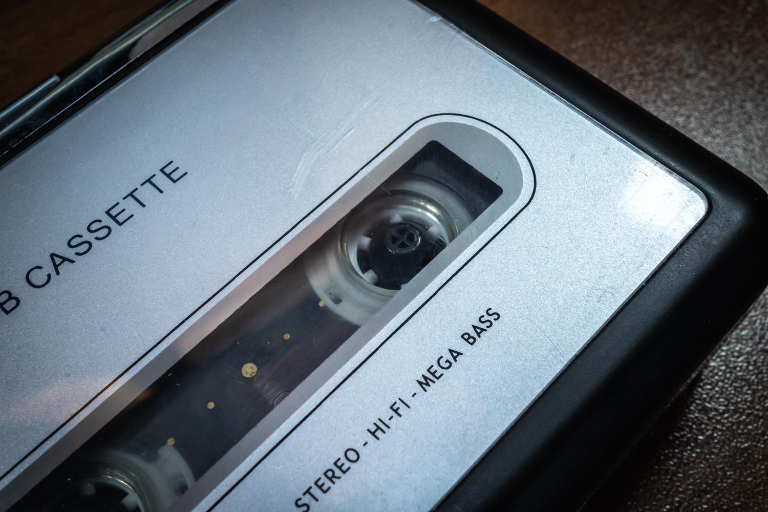 Nahaufnahme eines tragbaren, silberfarbenen Kassettenrekorders mit eingelegter Audiokassette. Durch das transparente Sichtfenster sind die Bandspulen und das Magnetband zu erkennen. Auf dem Gerät stehen die Aufschriften CASSETTE und STEREO-HI-FI-MEGA BASS. Der schwarze Rand des Geräts kontrastiert mit der metallischen Oberfläche.