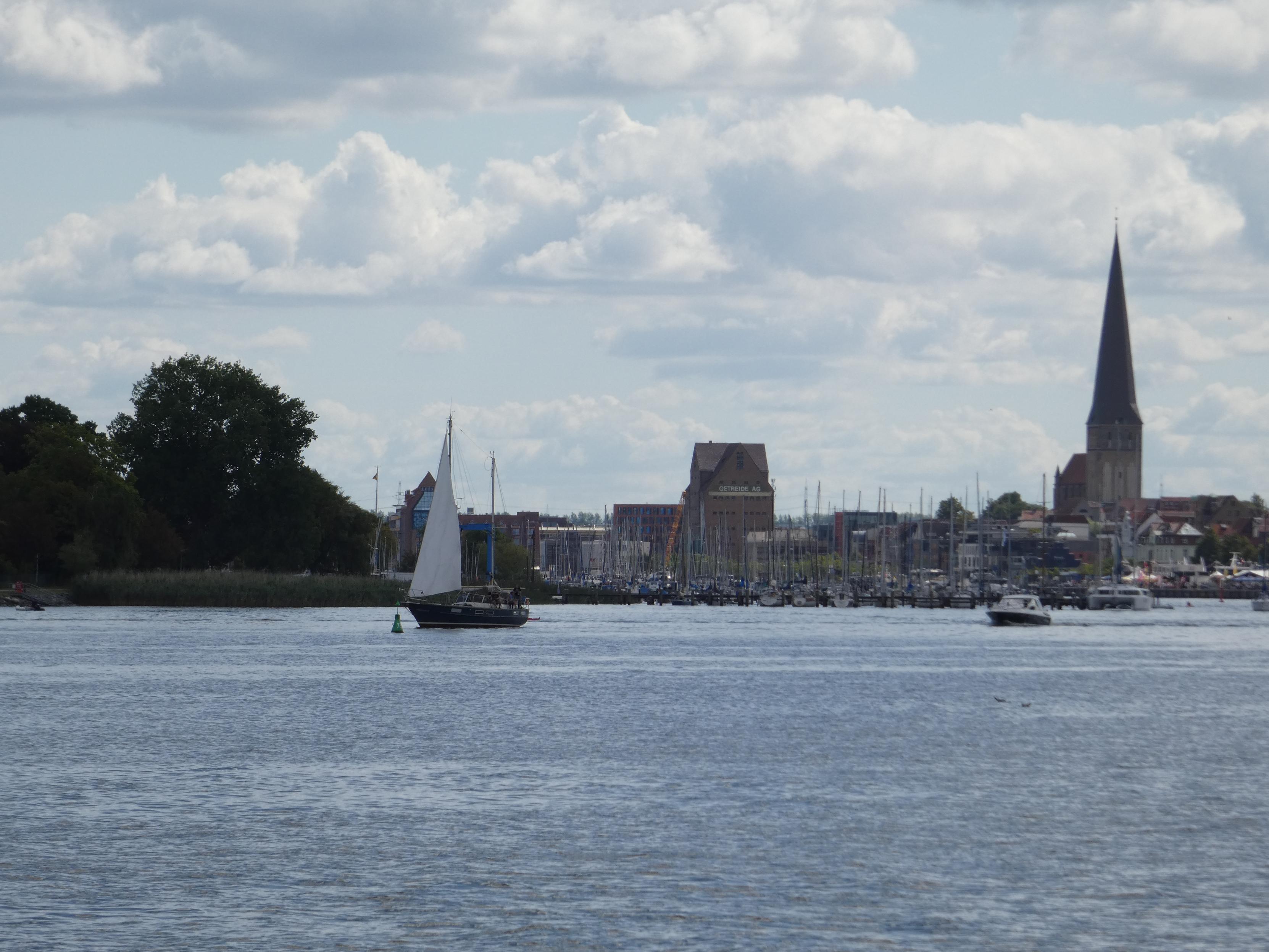 Die Rostocker Skyline mit links etwas Ufer bei Gehlsdorf. Ein kleines Segelschiff im Fokus. Rechts die Petrikirche. In der Mitte der Speicher. Vorne die Warnow.