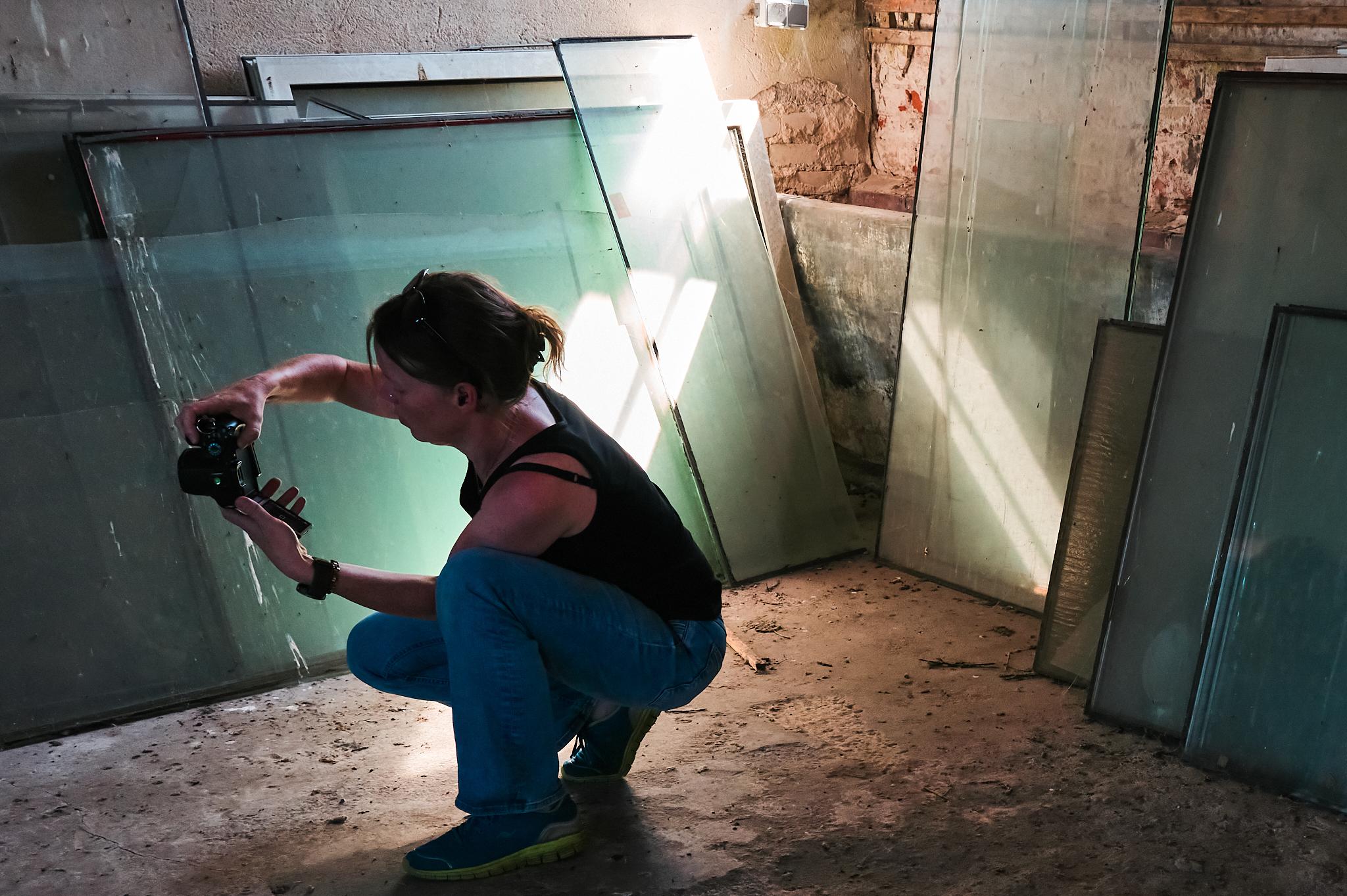 Anika fotografiert in einem Raum, im dem Glasscheiben und Fenster gelagert werden. Von schräg oben strahlt die Sonne in den Raum.