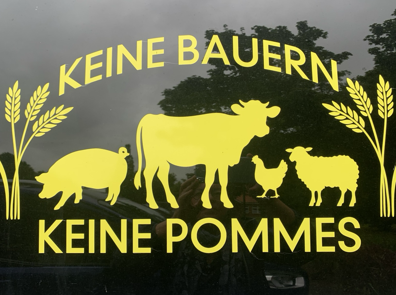 Ein Foto von einem Transporter in einer ländlichen Gegend, in gelb auf schwarz. „ Keine Bauern Keine Pommes“ mit Hoftieren und Getreideähren auch in Gelb auf Schwarz. 2O24