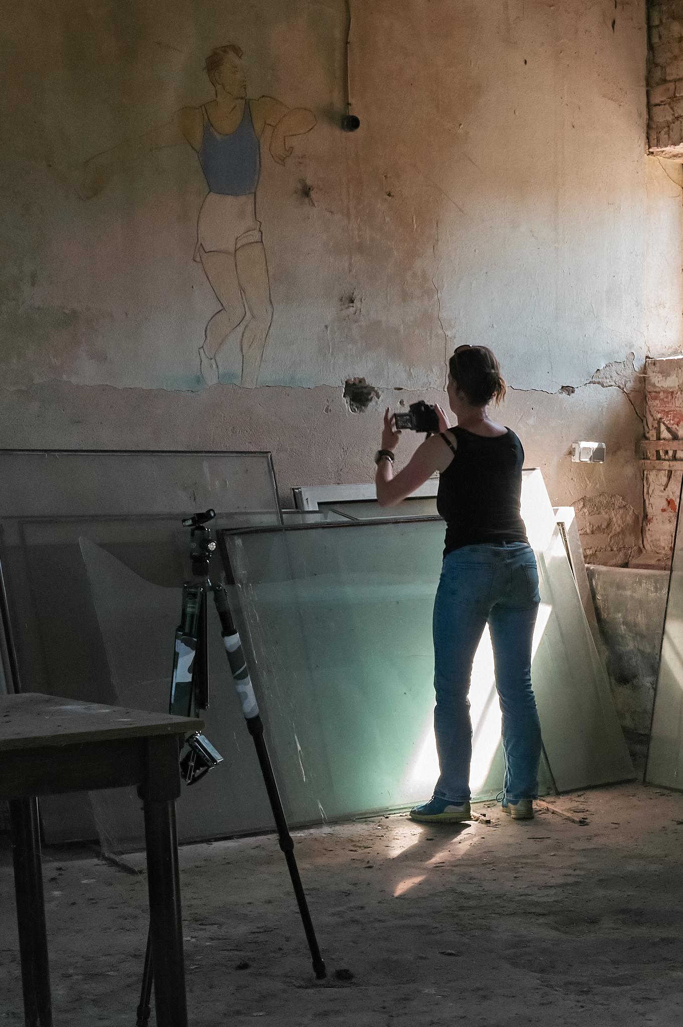 Eine junge Frau fotografiert in einem alten Lagerraum. Sie kehrt der Kamera den Rücken zu. Von der rechten Seite fällt Sonnenlicht in den Raum.