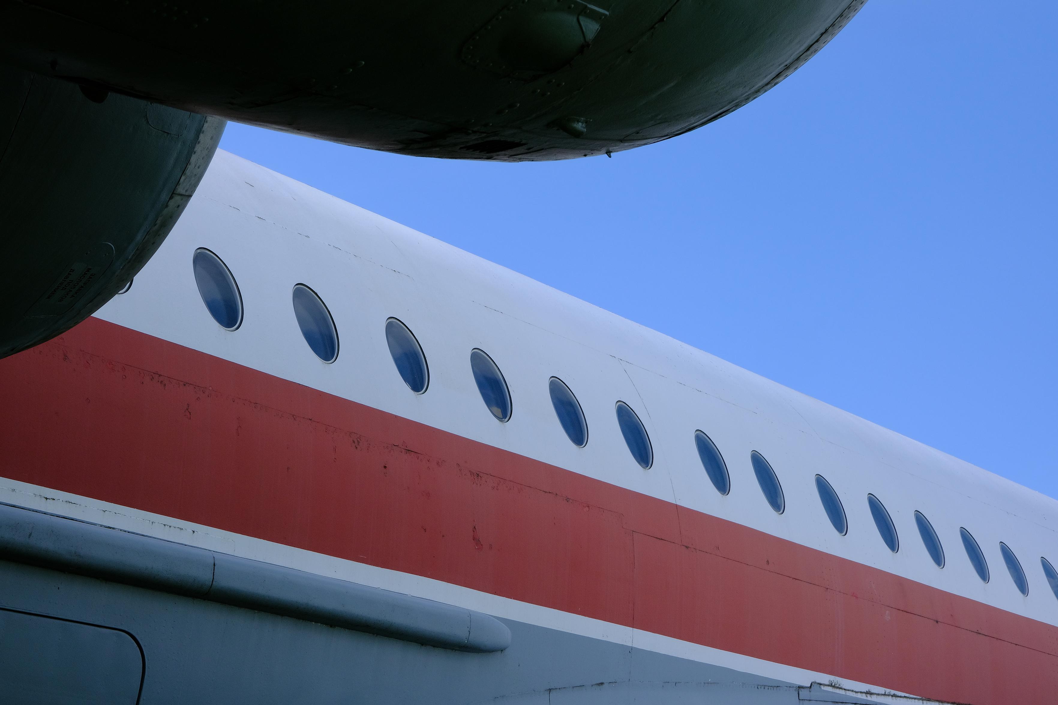 Blick auf die Fensterreihe eines rot-weißen Flugzeugs. Links oben als Schatten die Triebwerke