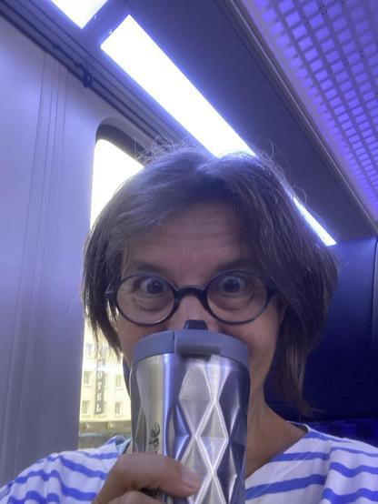 blaue Stimmung. Ich im blÀulich beleuchteten Zug, auf einem blauen Sitz, in einem blau geringelten T-Shirt. Vor mein Gesicht halte ich meinen Kaffeebecher.