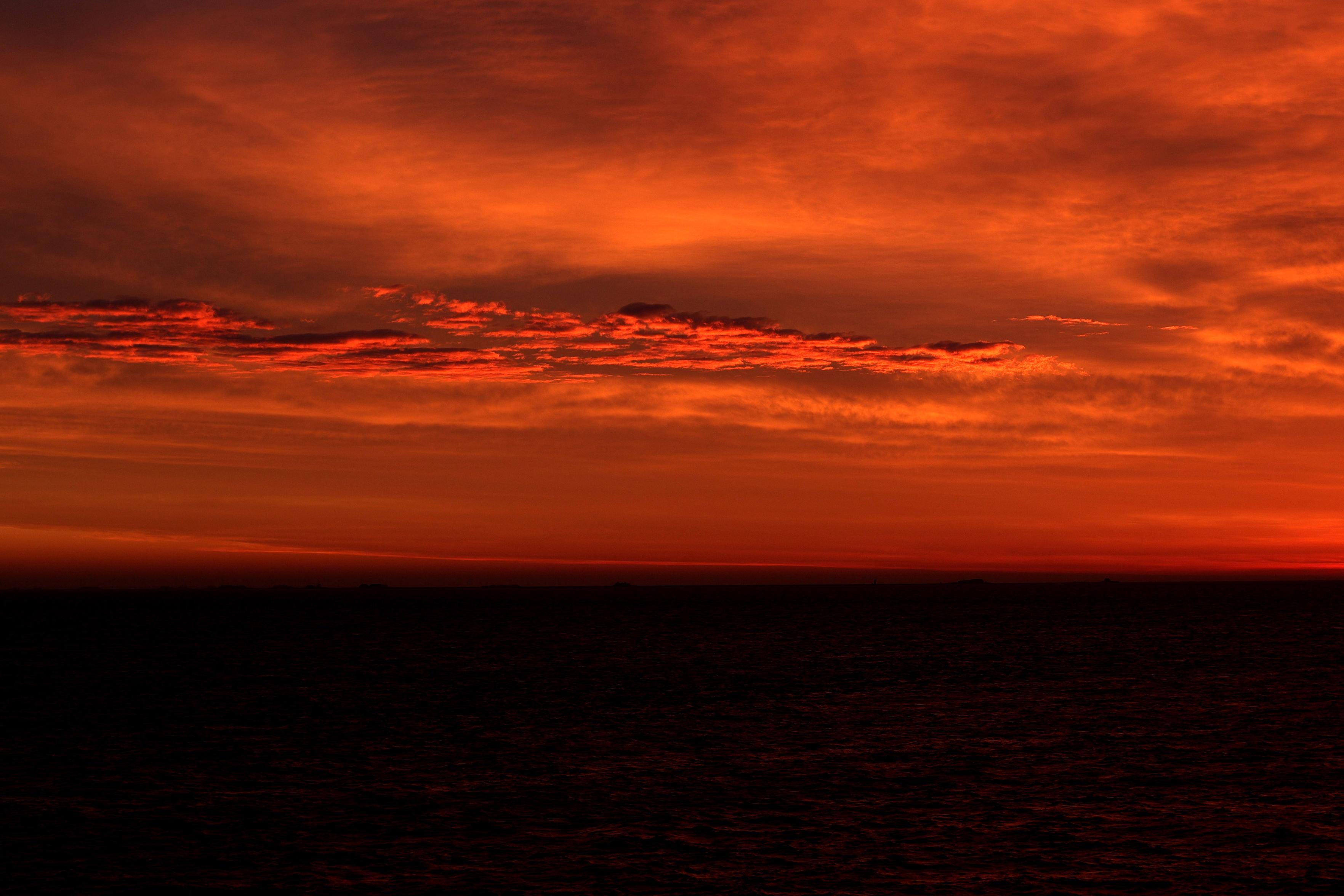 Auf der Fähre von Amrum zum Festland: Ein Sonnenaufgang über der Nordsee. Dunkelorangeroter Himmel mit Wolken, die Sonne wird gleich über dem Horizont aufgehen, die Farben sind intensiv. Die Nordsee ist dunkel, leichte Wellen, auf manche scheint schon etwas Licht. (Oktober 2025)

On the ferry from Amrum to the mainland: a sunrise over the North Sea. A dark orange-red sky with clouds; the sun is about to rise above the horizon; the colours are intense. The North Sea is dark, with gentle waves; some of them are already catching a little light. (October 2025)