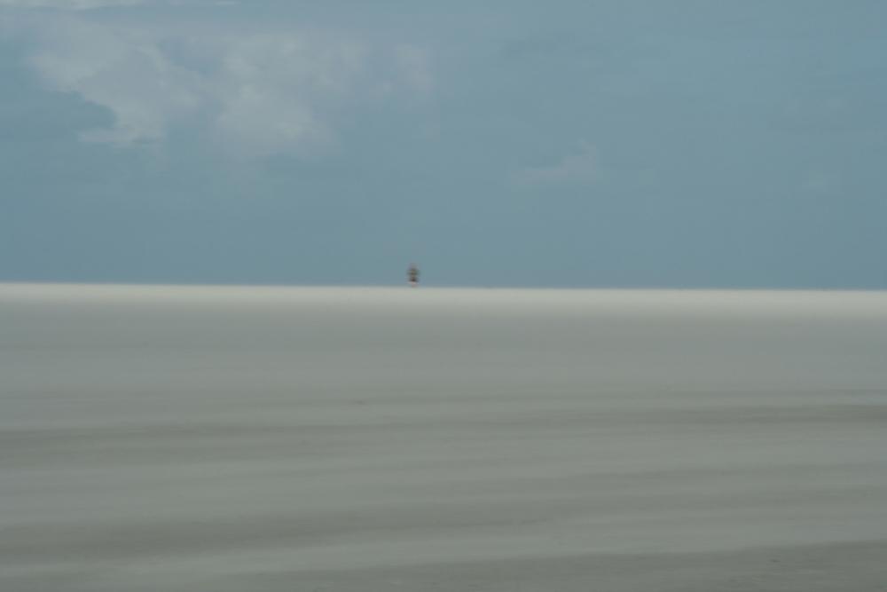 Like an illusion a lone person seems to emerge at the horizon - out of sand drifting on the beach.