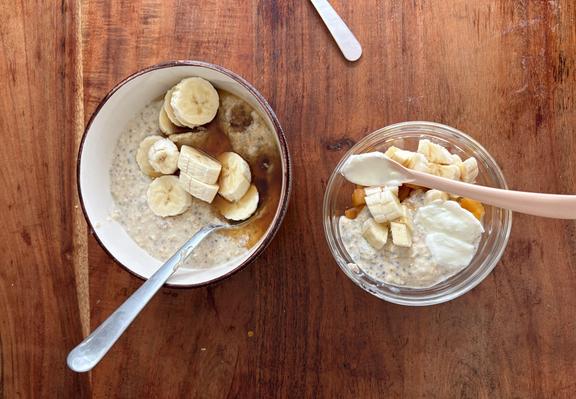 Zwei Schüsseln, ein kleine und eine große, mit Brei und Löffeln, Obst, Joghurt und die eine mit Sirup.