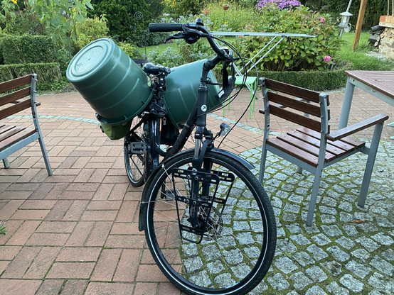 mein Rad von vorne. Es handelt sich um ein schwarzes TrekkingBike, hinter dem Sattel sind zwei riesige GartenTonnen links und rechts auf dem Fahrrad befestigt.