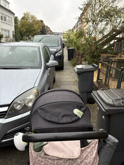 Ein schmaler Gehweg in Elbe Straße mit Reihenhäusern und Vorgärten. Bitte den Gästen stehen mobile Mülltonnen. Auf dem Gehweg abgestellte Autos machen die Restbreite zu schmal für den Kinderwagen auf dem Foto